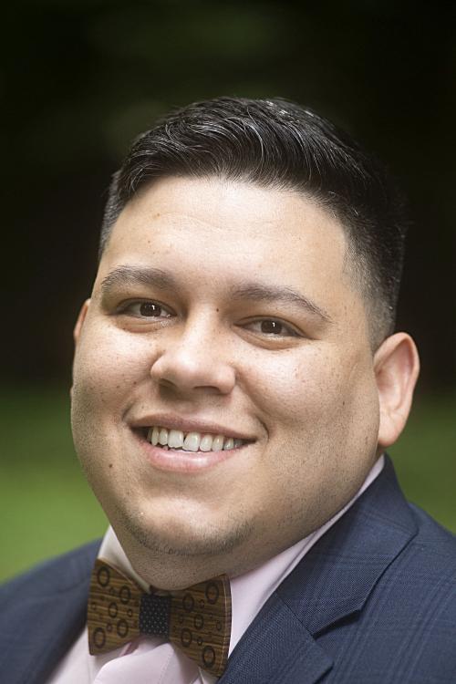 Man smiling with wearing a bowtie in front of a green background